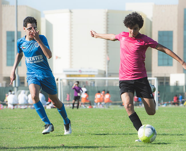 two young men playing soccer, one with glasses and one without