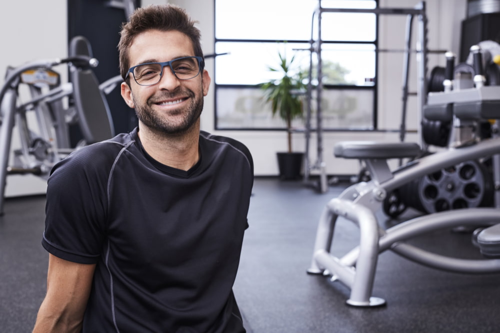 Fit man with glasses sitting in the gym smiling